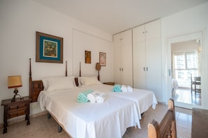 A hotel room with two beds, a nightstand, a lamp, and a view of the outside. - Perla 5 - Charming Front-Row Apartment (Fuengirola)