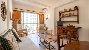 A living room with a sofa, chairs, a table, a TV, and a balcony with a view. - Perla 5 - Charming Front-Row Apartment (Fuengirola)