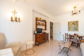 A living room with a television, wooden cabinet, wicker furniture, and a dining table with chairs. - Perla 5 - Charming Front-Row Apartment (Fuengirola)