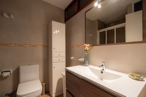 A modern bathroom with a toilet, a sink with a vase of flowers, and a mirror. - Perla 5 - Charming Front-Row Apartment (Fuengirola)