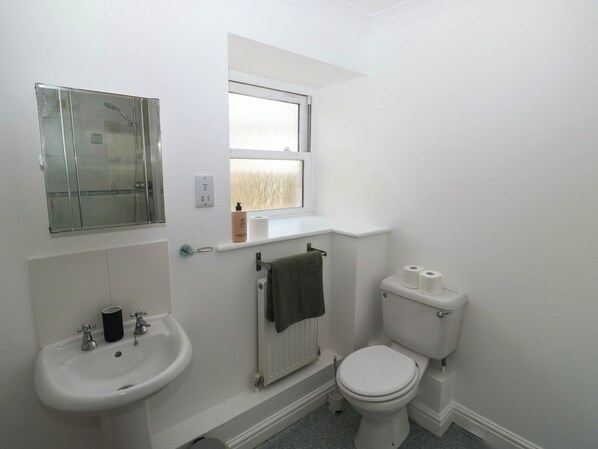 Un baño pequeño y blanco con lavamanos, inodoro y ventana sobre el inodoro.