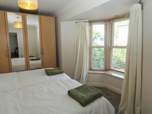 Een slaapkamer met een bed, een kledingkast, een raam met jaloezieën en een spiegel.