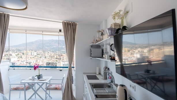 A modern kitchen with a large window, a dining area, and a view of a cityscape. - Hotel El Puerto - Perfect Location Apartment (Fuengirola)