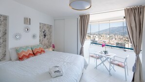 A bedroom with a bed, a small table with chairs, a view of the city, and a balcony. - Hotel El Puerto - Perfect Location Apartment (Fuengirola)