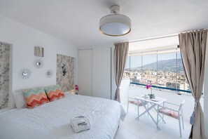 A bedroom with a bed, a small table with chairs, a view of the city, and a balcony. - Hotel El Puerto - Perfect Location Apartment (Fuengirola)