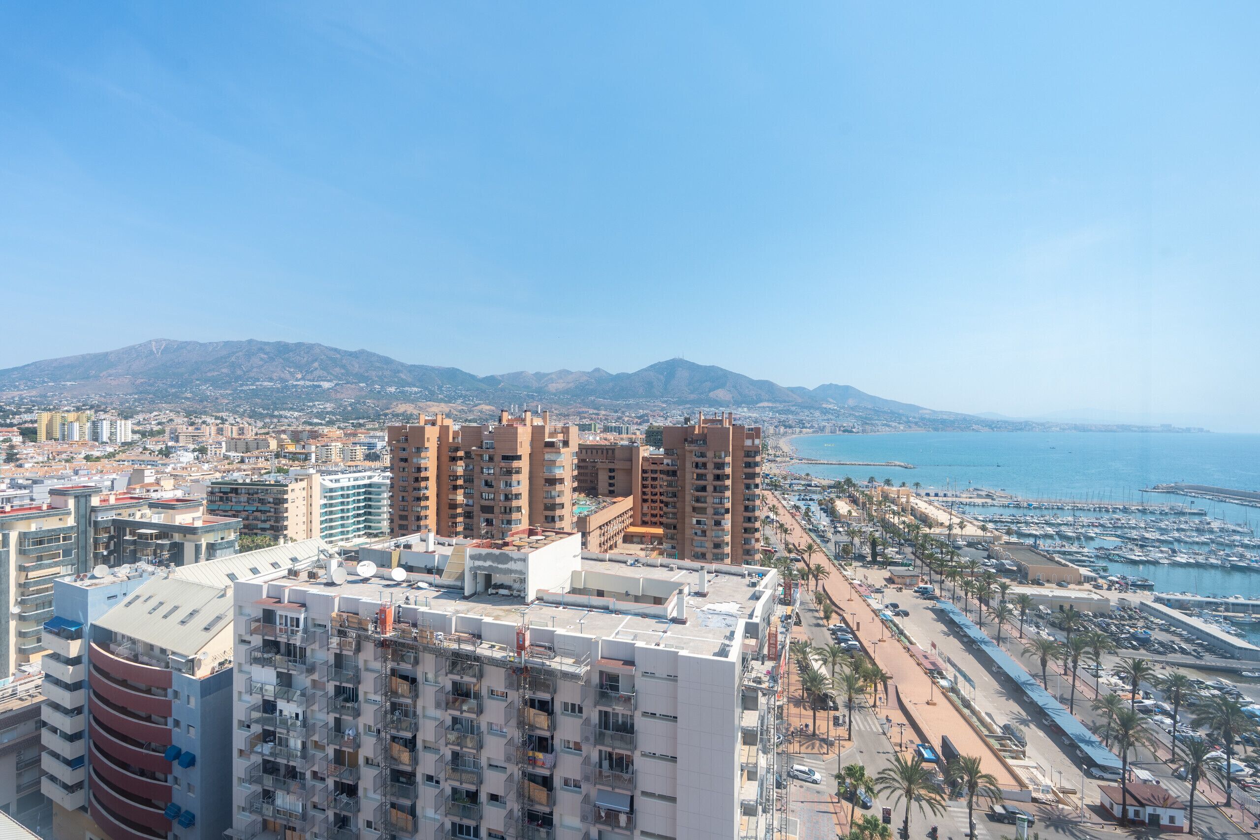 A coastal cityscape with high-rise buildings, a marina, and a clear view of the sea.