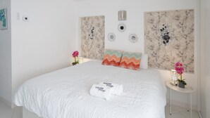 A hotel room with a large bed, a headboard with decorative panels, a bedside table with a lamp, and a small potted plant. - Hotel El Puerto - Perfect Location Apartment (Fuengirola)