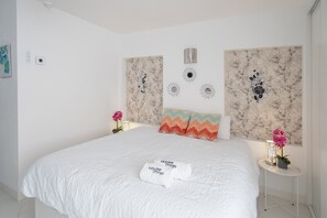 A hotel room with a large bed, a headboard with decorative panels, a bedside table with a lamp, and a small potted plant. - Hotel El Puerto - Perfect Location Apartment (Fuengirola)