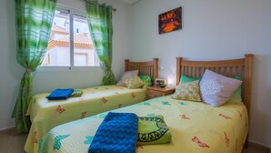 Un dormitorio con dos camas, cortinas verdes, un cuadro y una ventana con vistas a edificios.