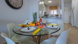 Un comedor con una mesa redonda de vidrio, sillas blancas y un reloj en la pared.