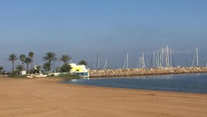 Una playa arenosa con cielo despejado, un vehículo amarillo y una hilera de embarcaciones blancas.