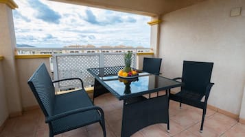 Un balcón con una mesa y sillas de vidrio, un frutero y vistas a edificios distantes.