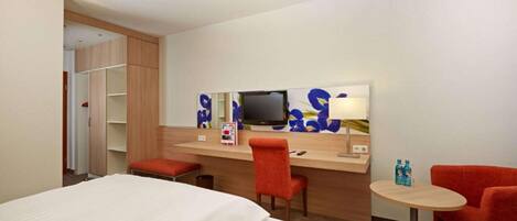 Habitación de hotel con cama, escritorio, silla, televisor y una pequeña mesa con botellas.