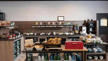 Un bufé de desayuno con diversos alimentos y bebidas, dispuesto en estantes y mostradores.