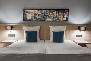Ein Doppelbett mit weißen und blauen Kissen, zwei Nachttische mit Lampen sowie ein gerahmtes abstraktes Gemälde über dem Bett.