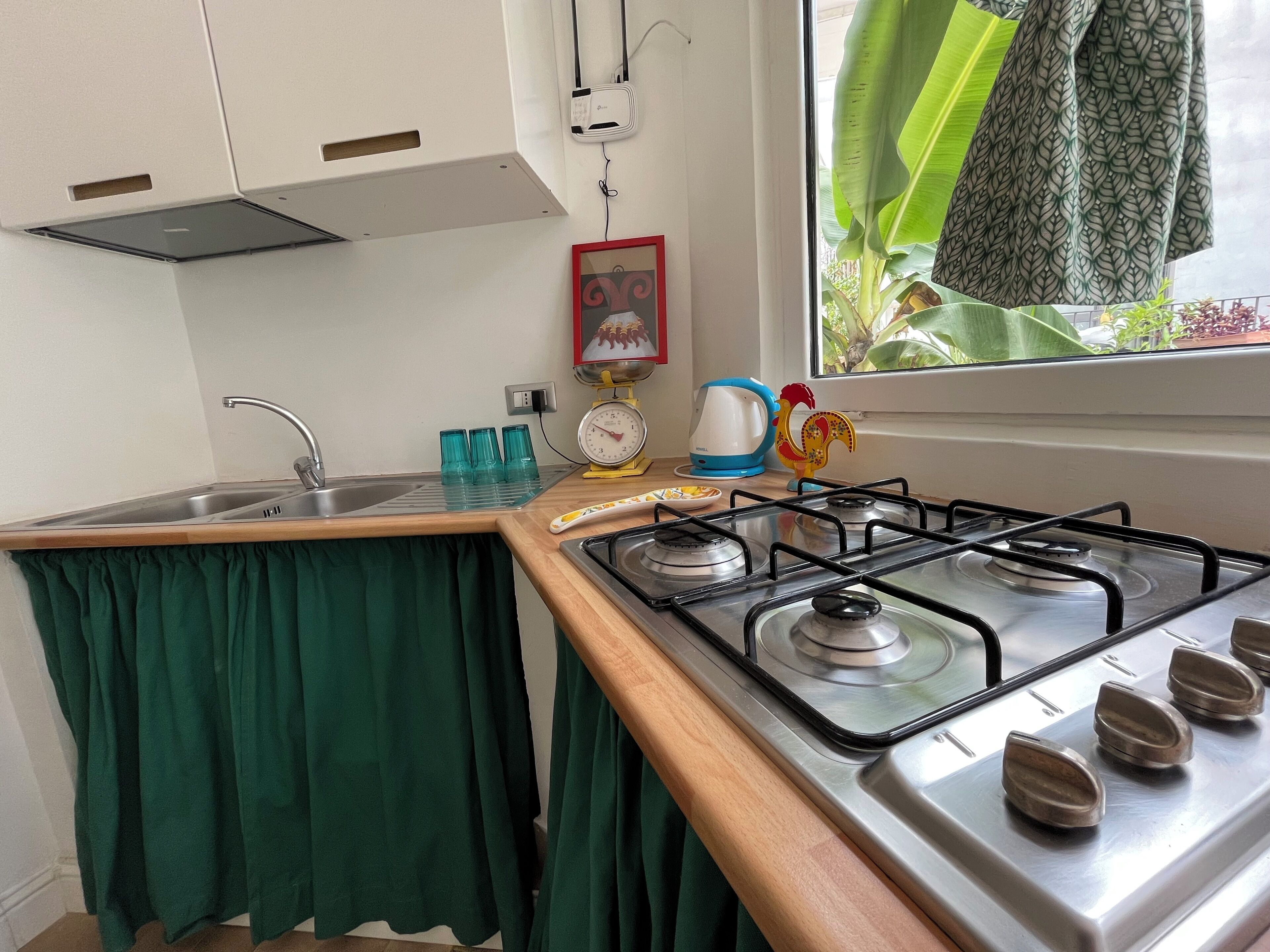 Una cocina con estufa a gas, lavamanos y ventana con vista a la vegetación.