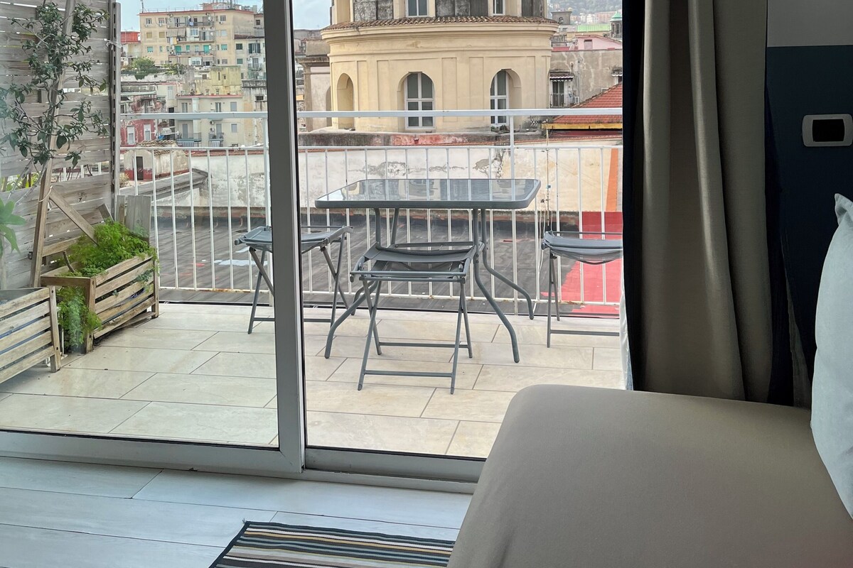 A balcony with a table and chairs, a view of a historic building, and a bed with a window.