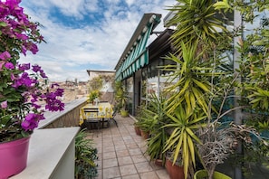 Eine Dachterrasse mit Tisch und Stühlen, umgeben von Blumentöpfen und Blumen.