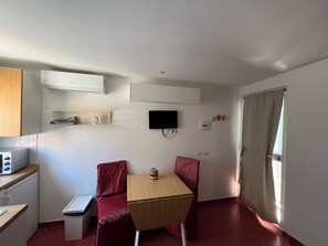 A compact room with a kitchenette, a single bed, a TV mounted on the wall, and a window with curtains. - Relais Tribunali with panoramic terrace (Napoli)
