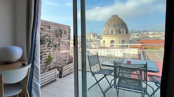 Una habitación moderna con un gran ventanal corredera que da a una terraza al aire libre. La terraza tiene una mesa con sillas y vistas a un edificio histórico con cúpula.