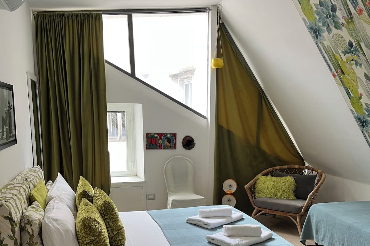 Un dormitorio con una cama, dos mesitas de noche, una silla, un ventanal y un ventilador de techo.