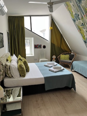 Ein Schlafzimmer mit einem Bett, zwei Nachttischen, einem Sessel, einem Fenster und einem Deckenventilator.