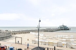 Ein Hotel am Strand mit einem Steg, der ins Meer führt, einem Rettungsschwimmturm und Strandstühlen.