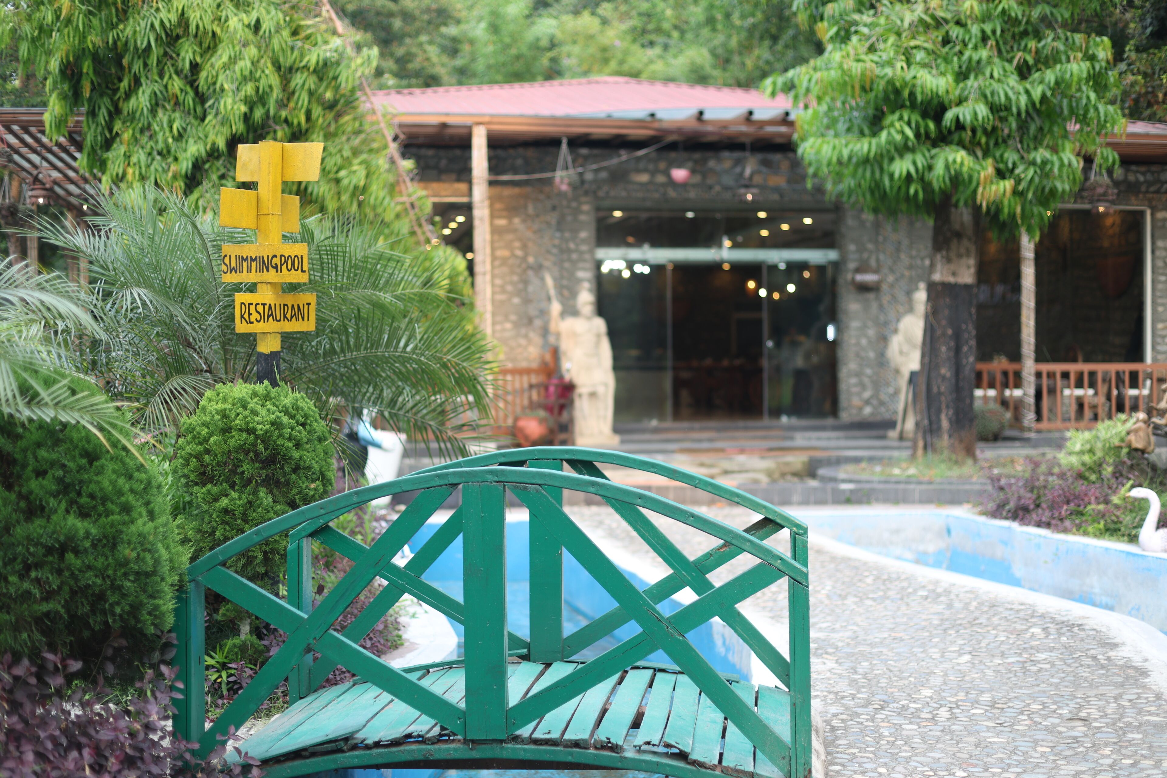 A green metal bench in a garden area with a sign indicating a swimming pool and restaurant nearby.