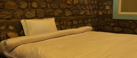 A bed with a white mattress and pillows, set against a stone wall.