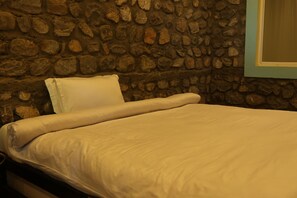 Una cama con colchón y almohadas blancas, frente a una pared de piedra.