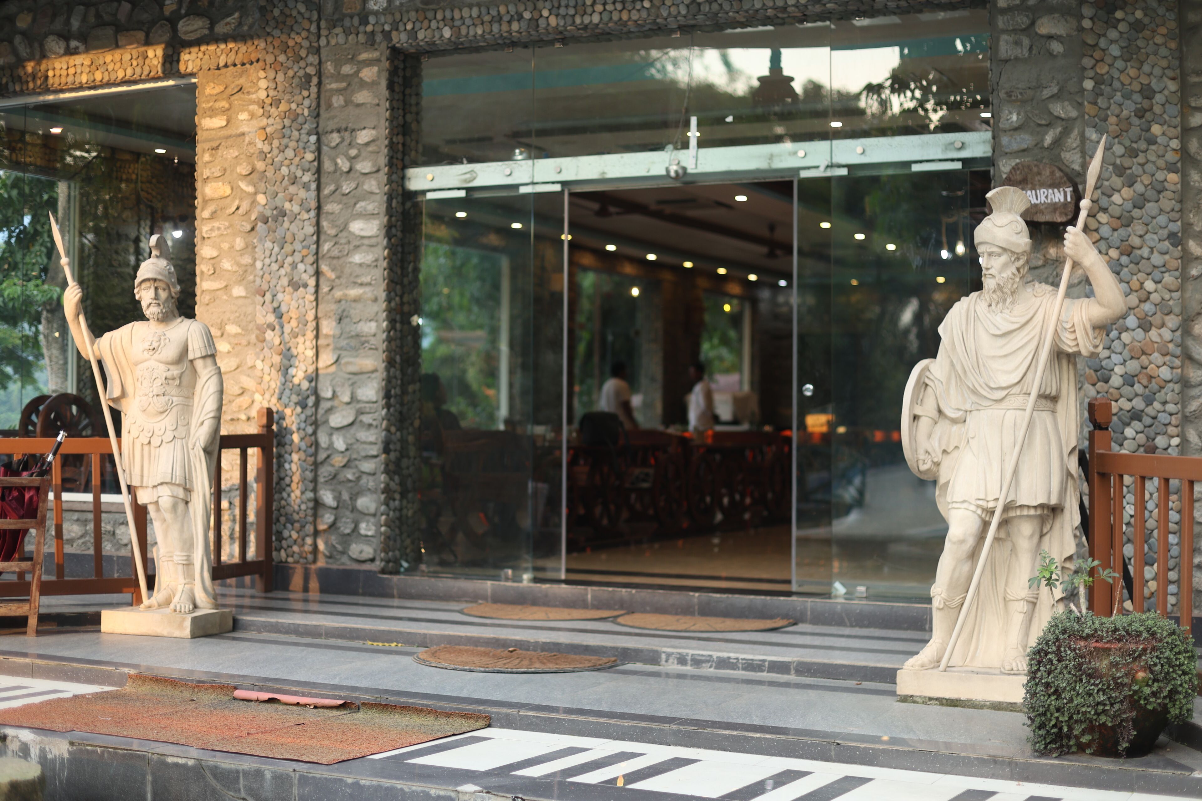 A building entrance with stone pillars, a statue of a figure holding a staff, and a sign that reads 'RESTAURANT'.