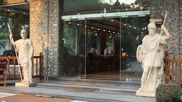 Fachada de edificio con pilares de piedra, una estatua de una figura sosteniendo un báculo, y un letrero que dice 'RESTAURANT'.