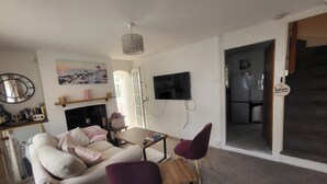 Una sala de estar con un sofá, dos sillones, una mesa de centro, una chimenea, un televisor y una puerta que da a la cocina.