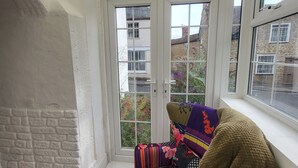 Un invernadero con una silla y un tapete, una pared de piedra y vistas a edificios.