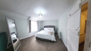 Un dormitorio con cama, mesita de noche, espejo y puerta.