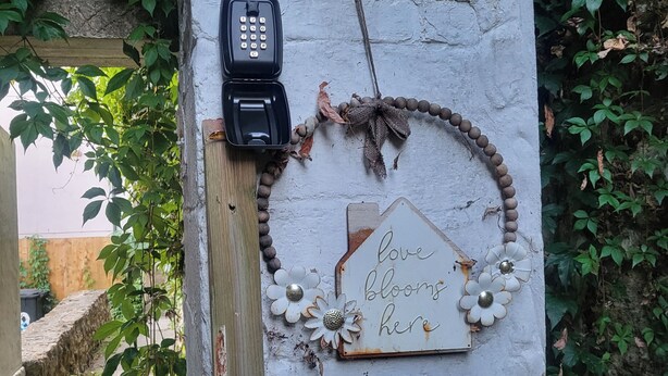 Un poste de madera rústico con un cartel desgastado que dice 'love blooms here' y un teléfono.