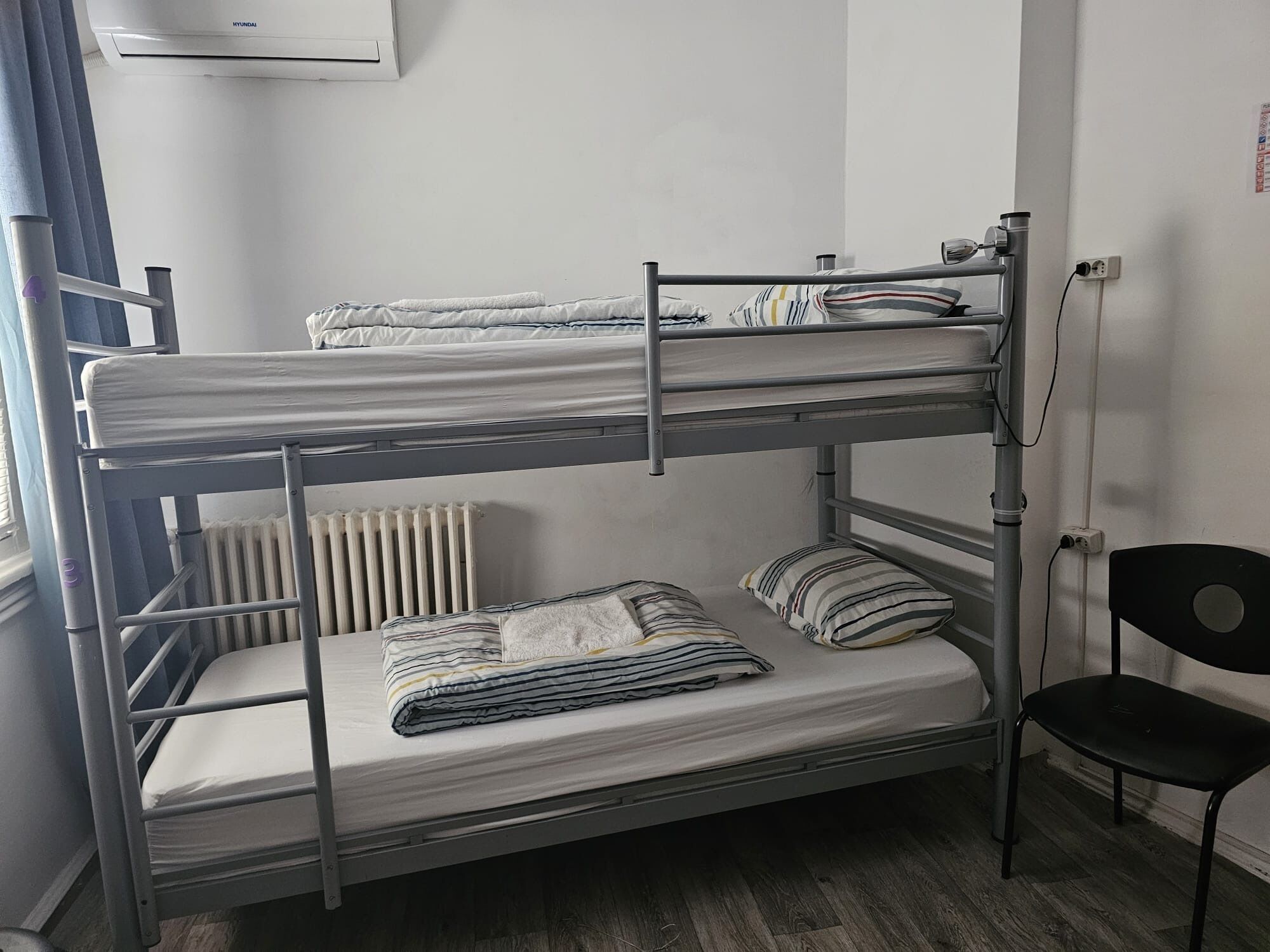 Dormitorio con literas, un radiador, una silla y aire acondicionado.