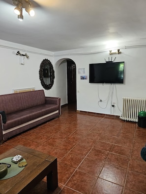 A living room with a sofa, a coffee table, a TV mounted on the wall, and a radiator. - Hostel Sport Bucharest (Bucharest)