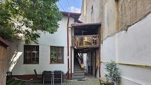 Une cour intérieure avec un escalier menant à un balcon en bois, le tout entouré d’immeubles.