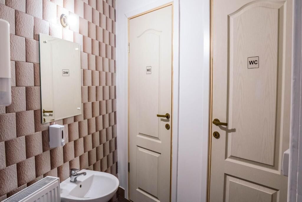 A bathroom with a tiled wall, a sink, and two doors marked 'WC'.