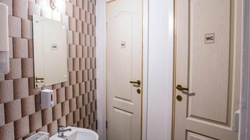 A bathroom with a tiled wall, a sink, and two doors marked 'WC'.