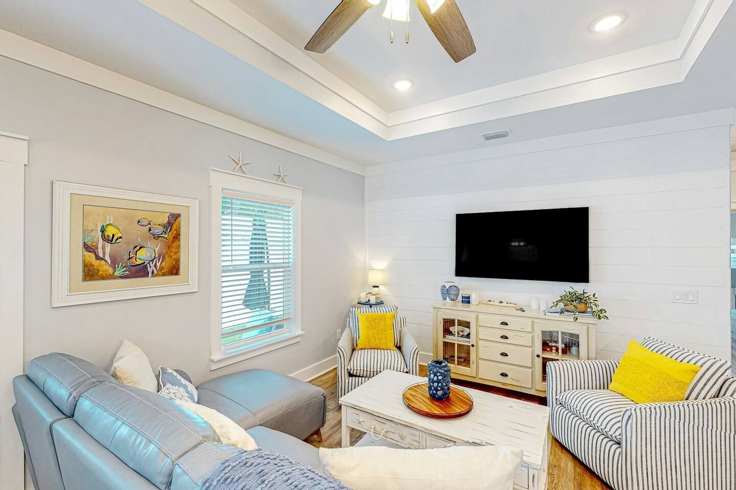 A living room with a sofa, armchair, and a TV mounted on the wall.