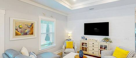 A living room with a sofa, armchair, and a TV mounted on the wall.