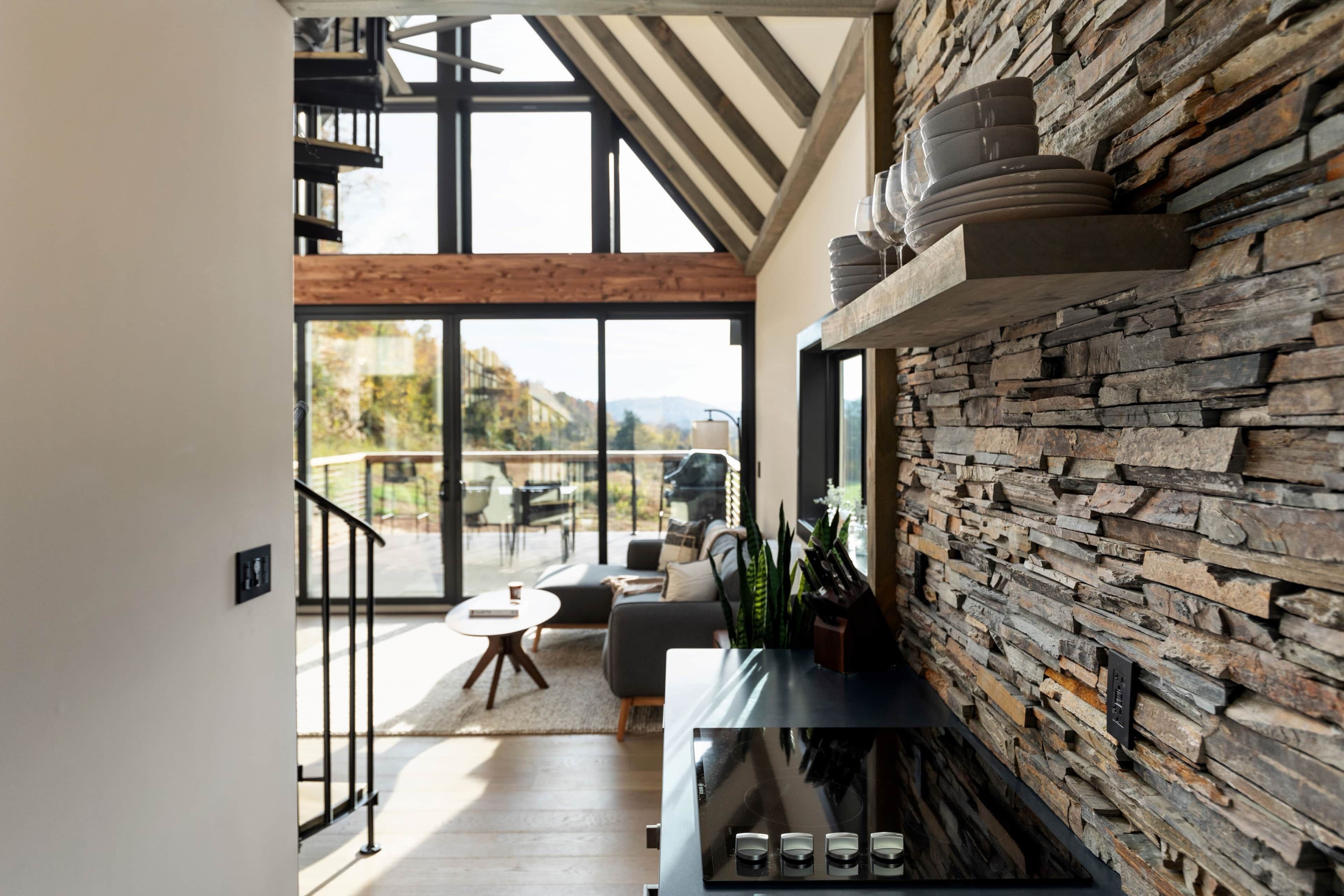 A modern interior with a stone wall, a staircase, and a view to the outdoors.