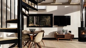 A modern living room with a dining area, a fireplace, and a large window with a forest view. - The Lakeside Cabin at Arete (Page County)