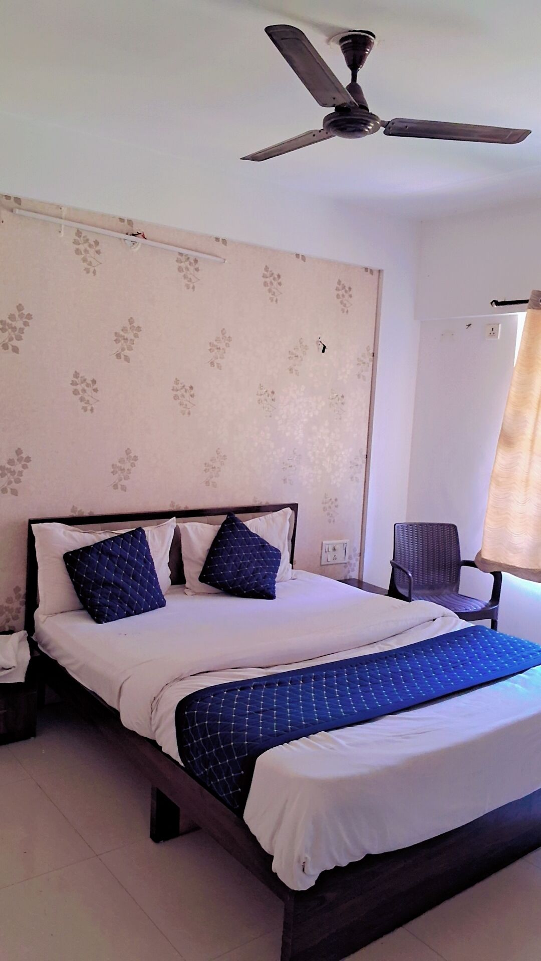 A bedroom with a bed, a chair, a ceiling fan, and a window with curtains.