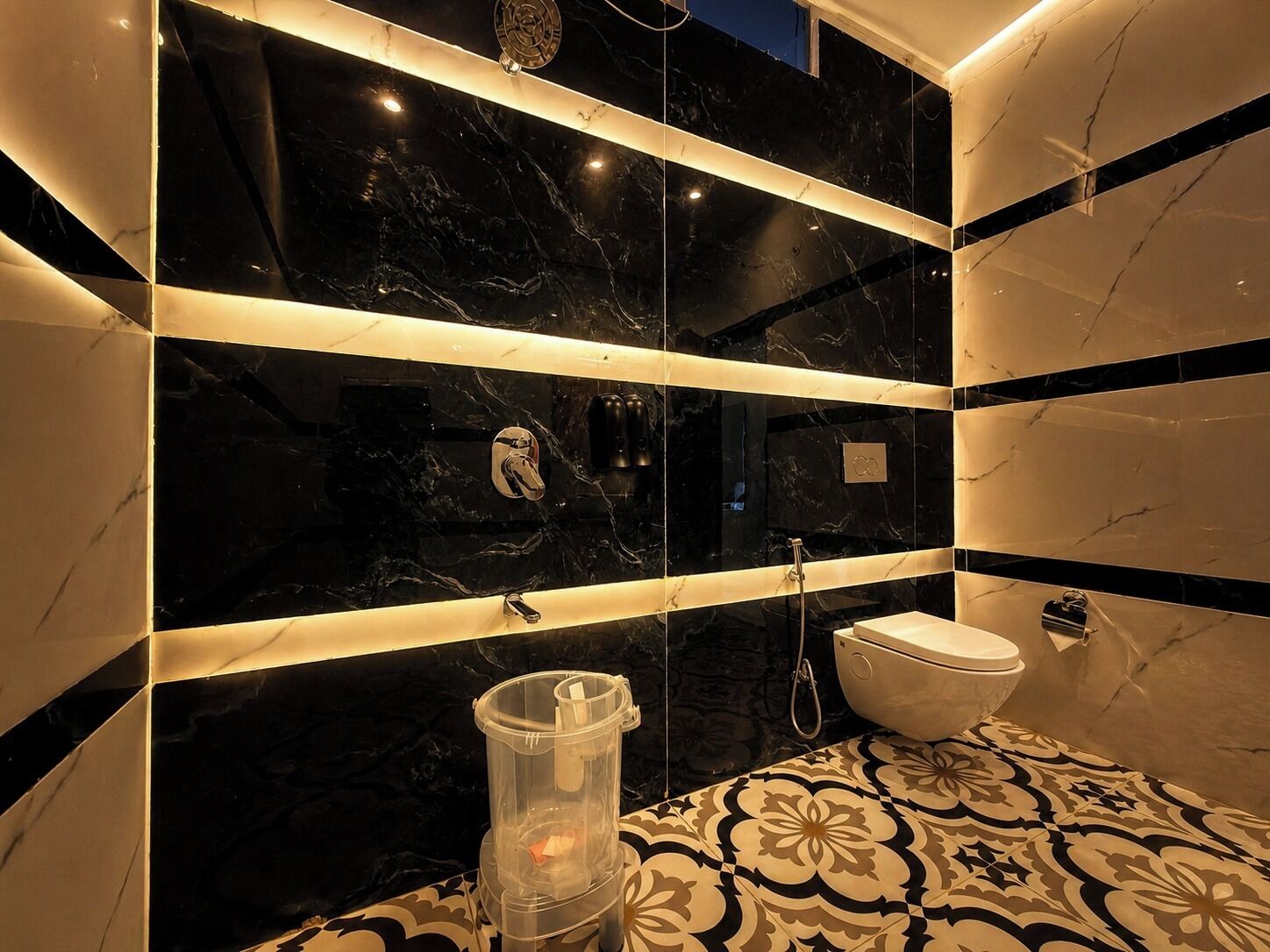 Un baño con azulejos de mármol blanco y negro, un inodoro, una ducha y un cubo de basura.