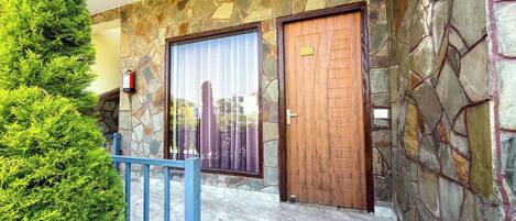 Fachada de pedra com porta de madeira e porta de vidro, portão de metal azul e um arbusto verde.