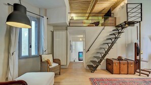 Ein großzügiger Wohnbereich mit Treppe, einer Couch, einem Korbstuhl und einem gemusterten Teppich.