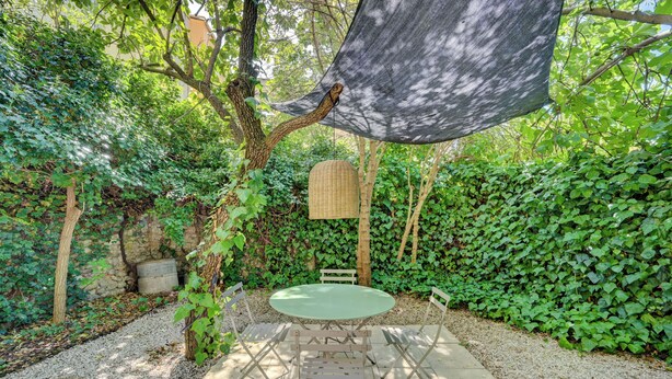 Eine Gartenpatio mit einem runden Tisch und Stühlen, umgeben von dichtem Grün und einem hängenden Korb.